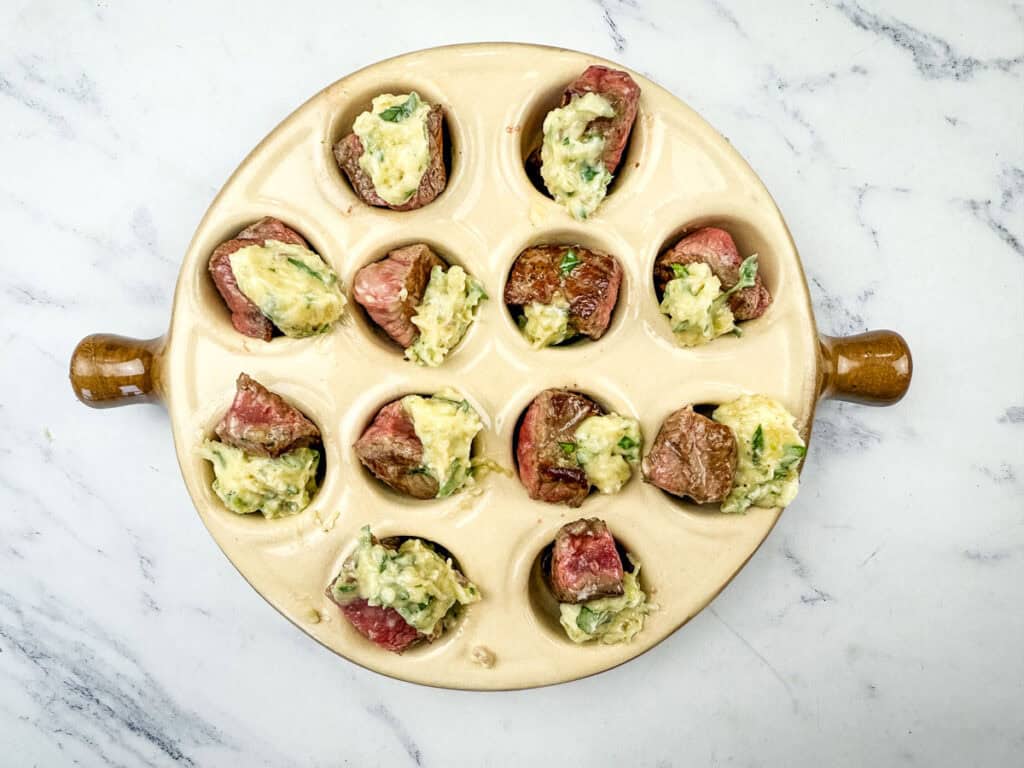 A steak bite on top with the butter mixture into each well of the escargot dish.
