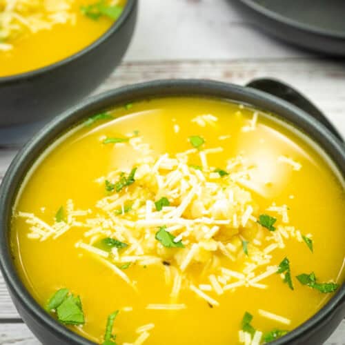 A bowl of Nonna’s pastina soup topped with shredded cheese and herbs.