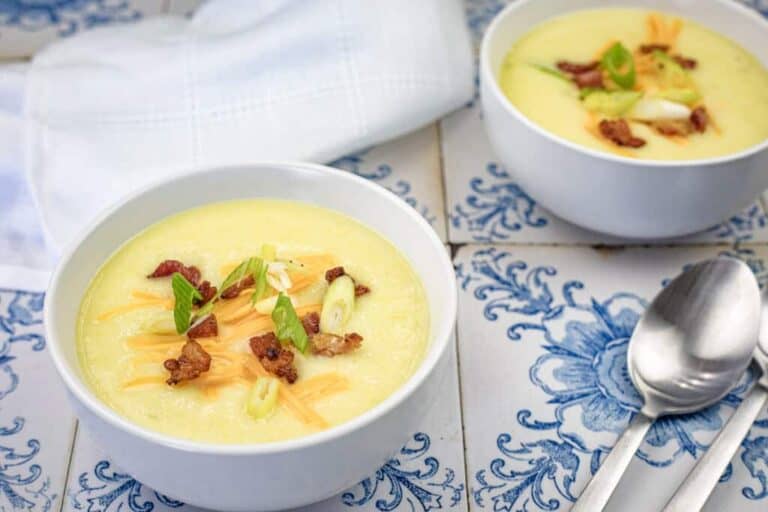 Two bowls of potato soup topped with cheese, bacon, and green onions on a patterned tile surface.