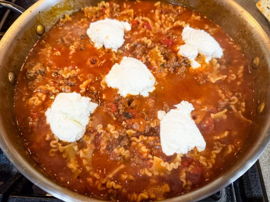 Skillet Lasagna topped with ricotta and mozzarella cheese on a stovetop.