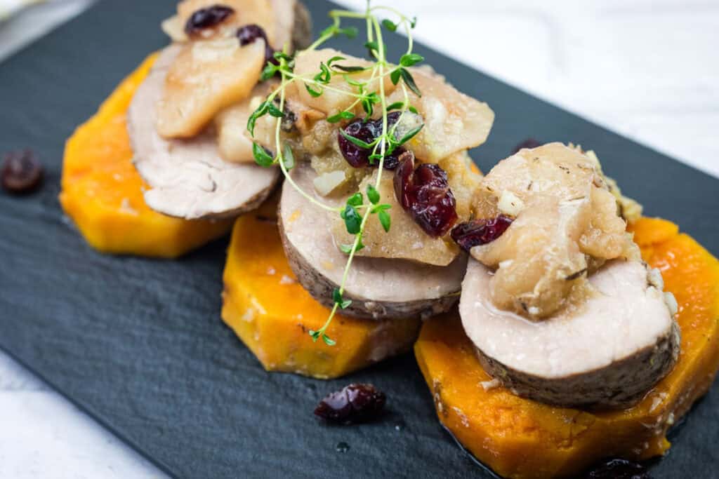 A serving of Slow Cooker Pork Tenderloin with Sweet Potatoes & Apples on a black platter.