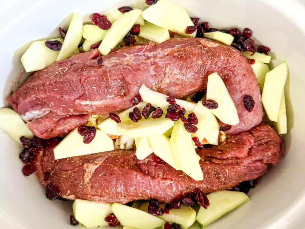 Nestle the apple wedges and dried cranberries around the pork.