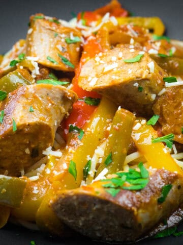 Slow cooker sausage and peppers garnished with grated cheese and chopped parsley.