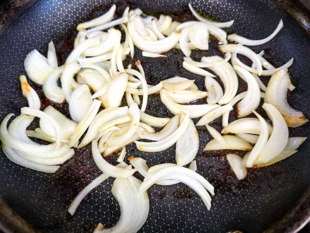 Sliced onions being sautéed in a frying pan.