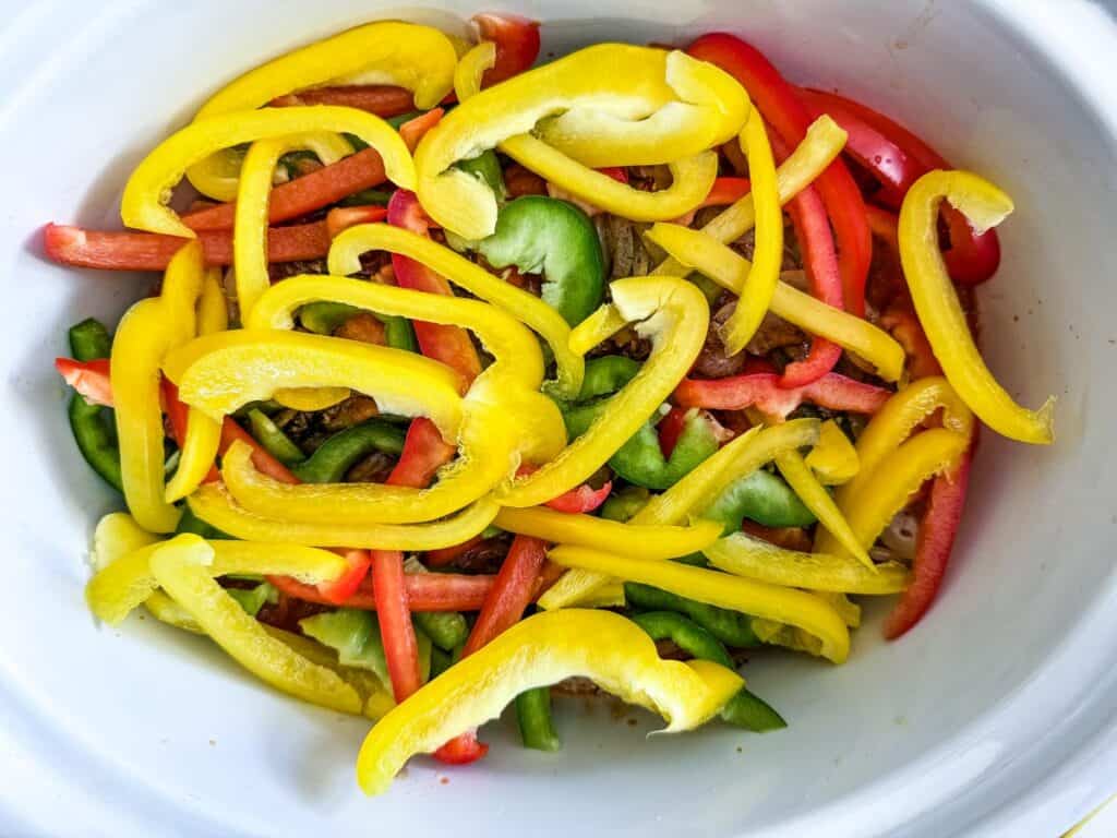Sliced yellow, red, and green bell peppers in a white bowl.