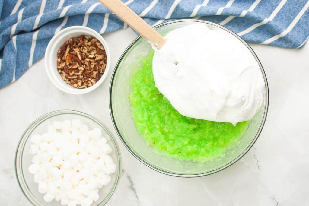 A bowl of pistachio mix, crushed pineapple and a bowl of pecans, and marshmallow on the side.