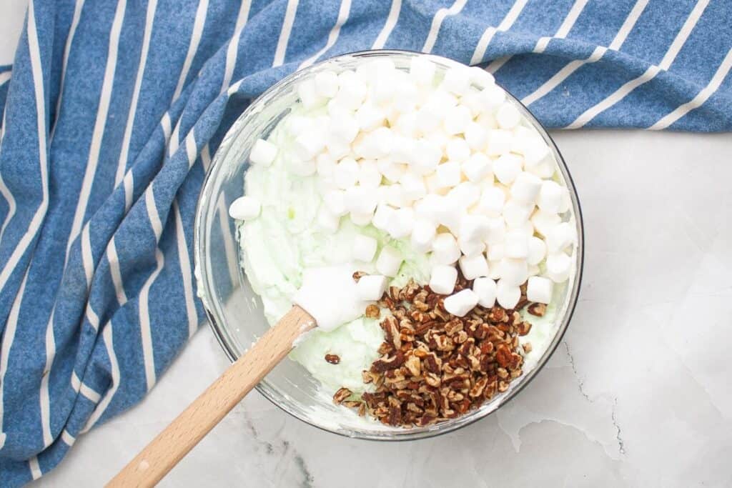 Mini marshmallows and chopped pecans mixed with pudding mixture in a bowl.