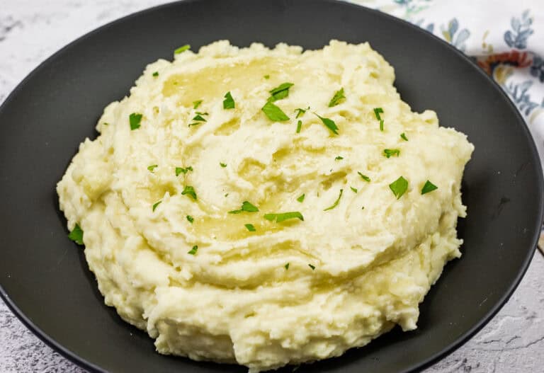 A black bowl filled with Grandma’s mashed potatoes topped with chopped parsley.