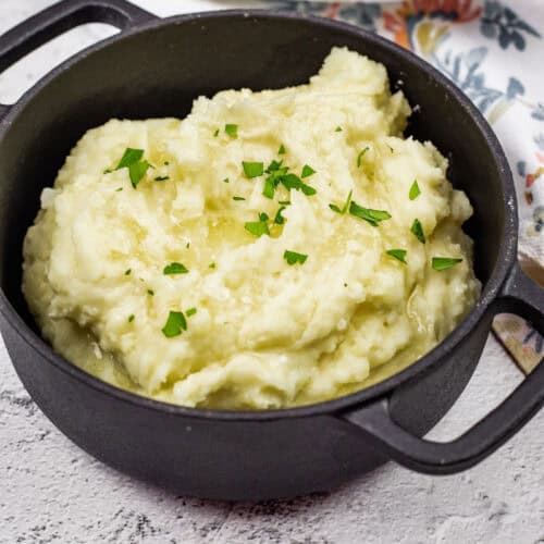 A black pot filled with Grandma's mashed Potatoes, garnished with chopped parsley.