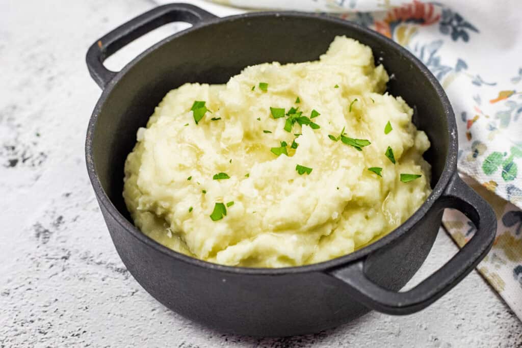 A black pot filled with Creamiest mashed potatoes, topped with chopped parsley.