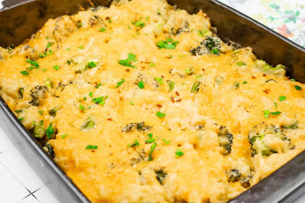 A baked Broccoli Rice Casserole dish with melted cheese, broccoli, and garnished with parsley, in a rectangular black baking pan.