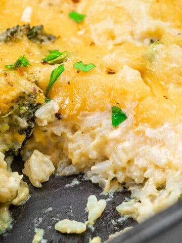 Close-up photo of a Broccoli Rice Casserole with a portion missing, garnished with parsley in a baking dish.