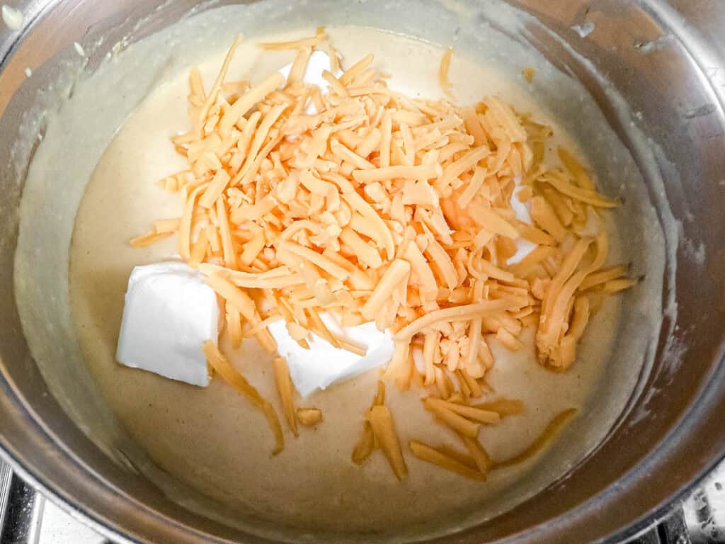 A saucepan filled with creamy sauce, shredded cheddar cheese, and cream cheese cubes.