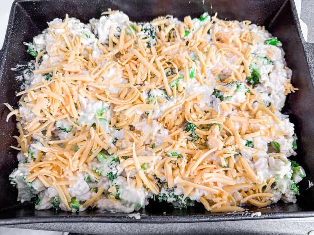 Casserole dish with uncooked broccoli, chicken, and shredded cheese mixture.