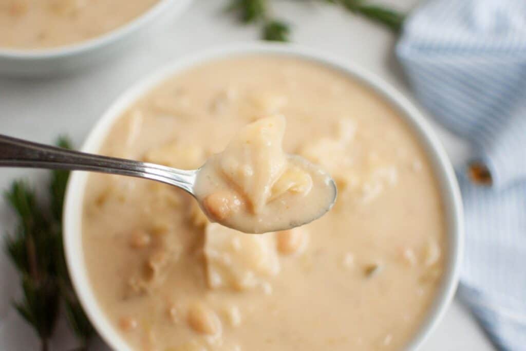 A spoonful of creamy cabbage and white bean soup is held above a bowl.