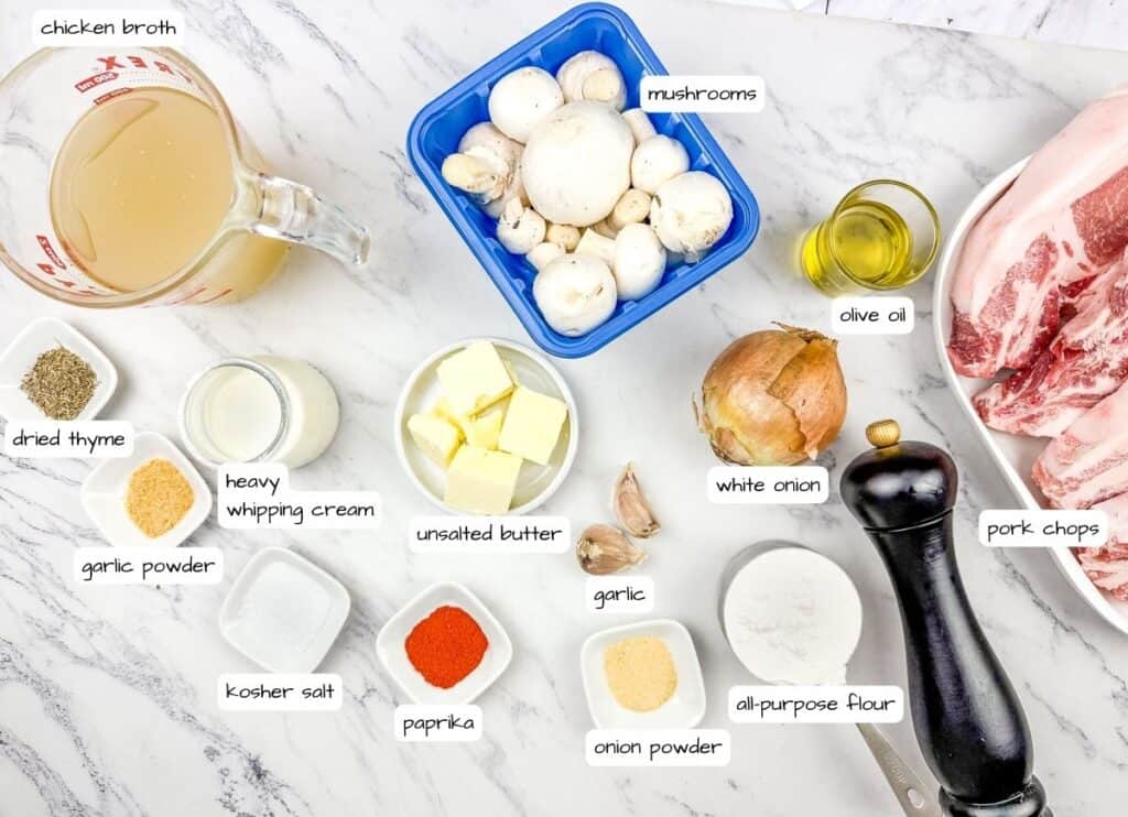 Ingredients for Cast Iron Smothered Pork Chops are arranged on a marble surface with label.