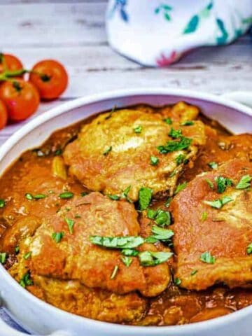 Baked chicken with tomato sauce and herbs in a white serving platter.
