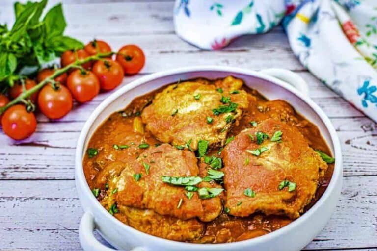 Baked chicken with tomato sauce and herbs in a white serving platter.