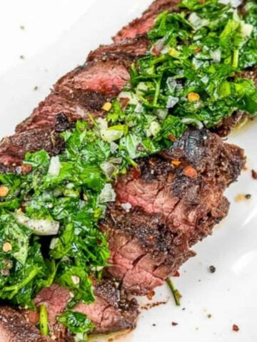 A plate of sliced Grilled Hanger Steaks with Chimichurri, served on a white rectangular dish.