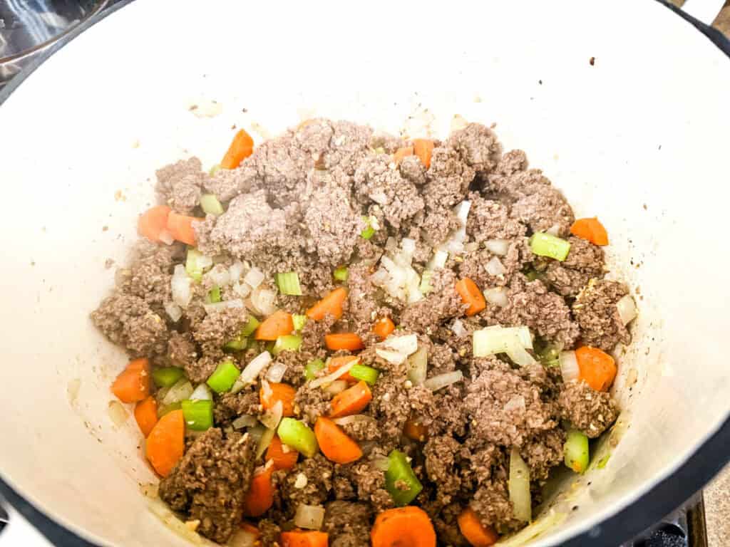 Ground beef, chopped carrots, celery, and onions cooking in a pot.