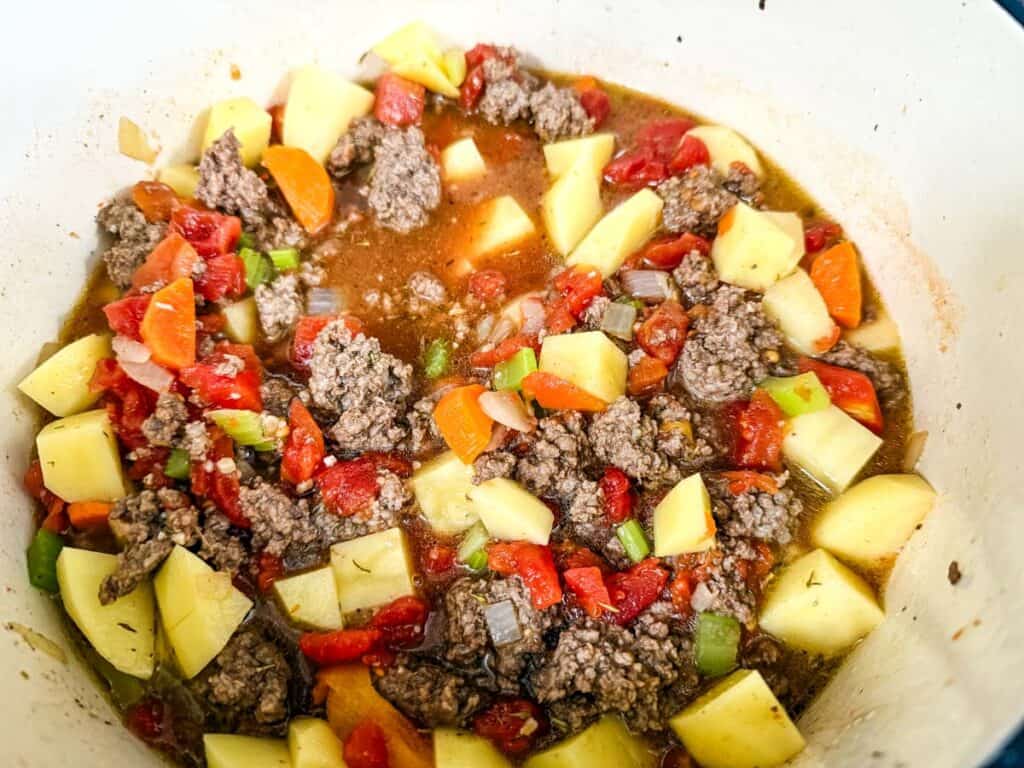 A pot containing a stew with ground meat, diced potatoes, carrots, celery, and tomatoes in broth.