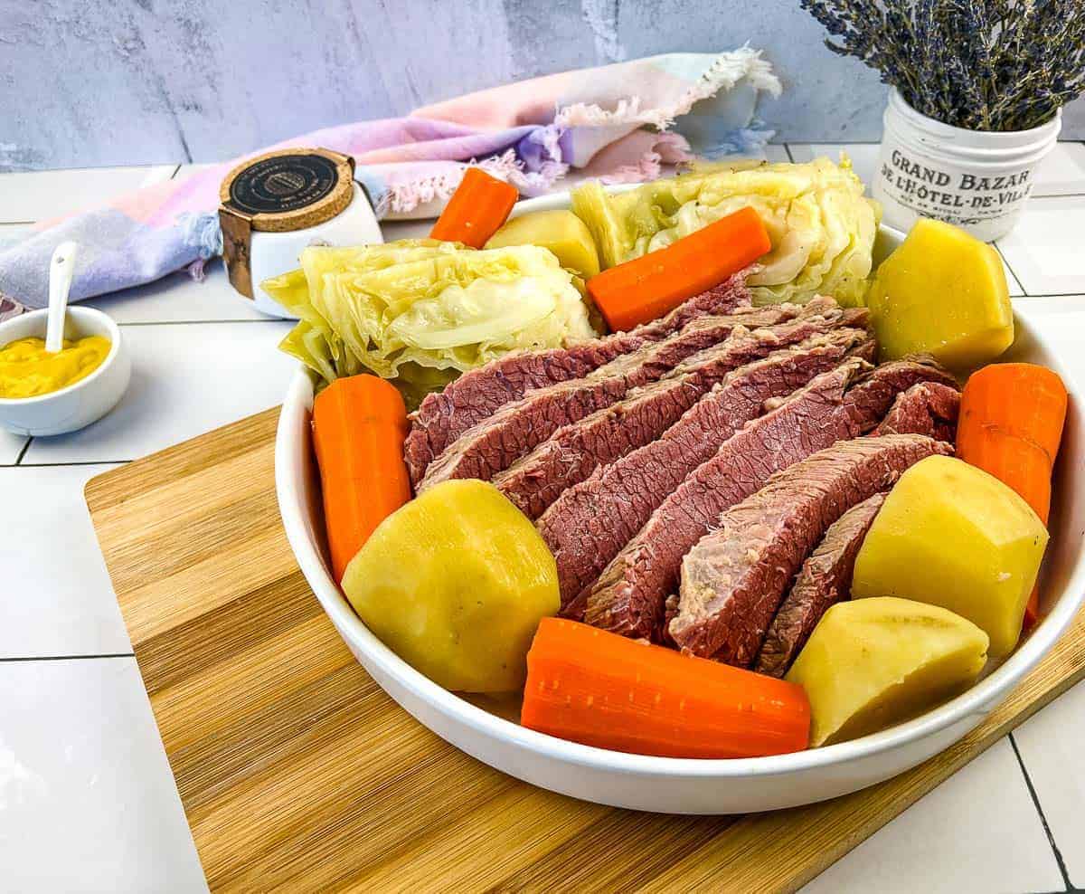 A bowl of corned beef and cabbage on a wooden cutting board with vegetables.