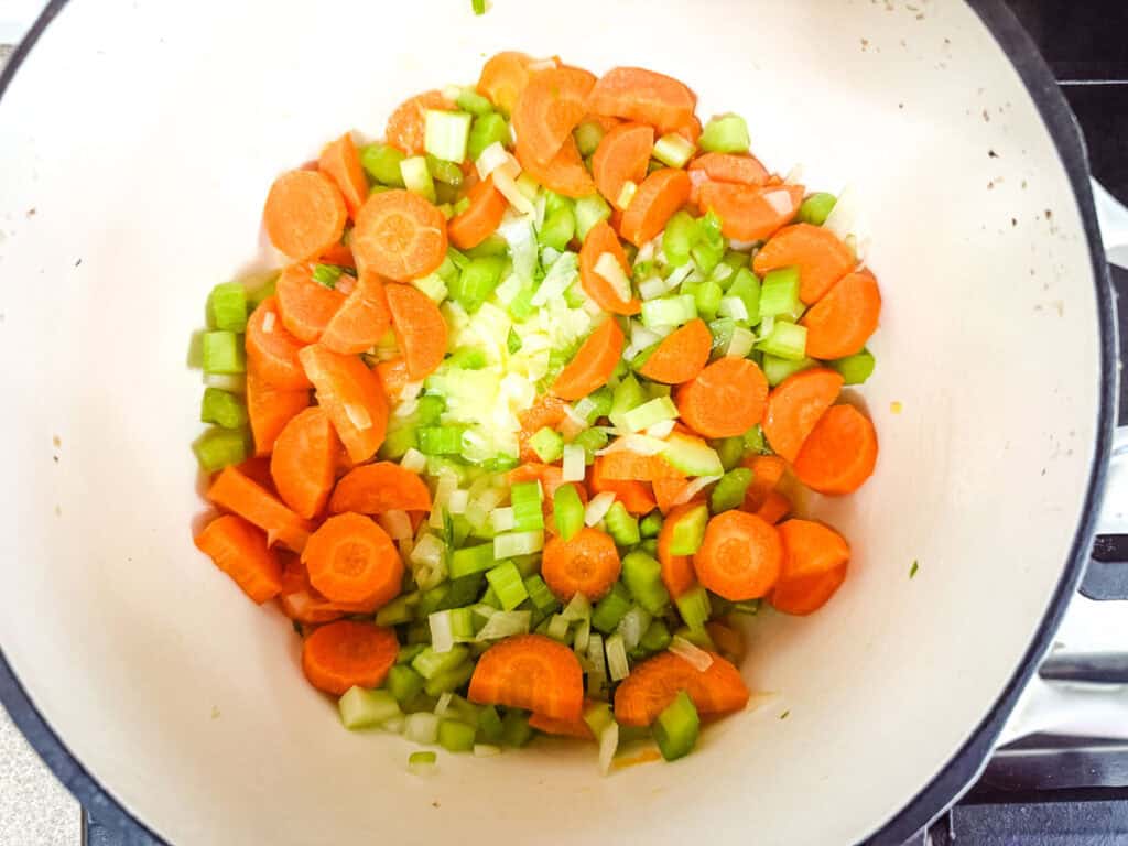 Chopped carrots, celery, and onions in a white pot on a stovetop.