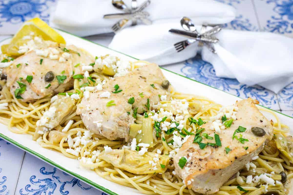 A dish of pasta topped with Skillet Chicken with Artichokes, Lemon, and Feta garnished with parsley.