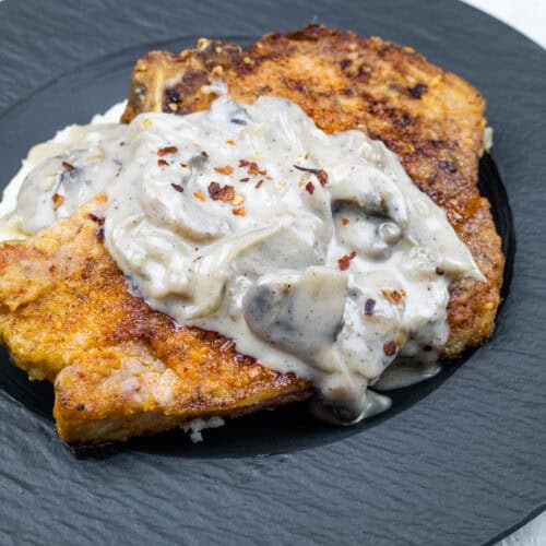 Serving of Cast Iron Smothered Pork Chops in a black plate.