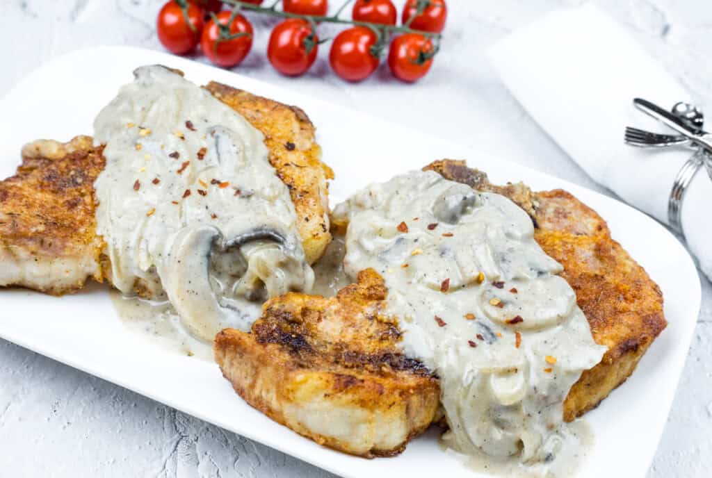 A serving of two Cast Iron Smothered Pork Chops on a white rectangular plate.