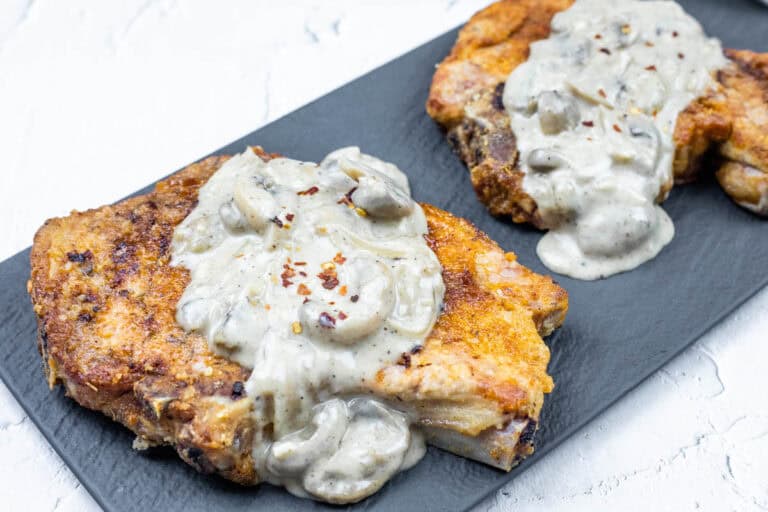 A serving of two Cast Iron Smothered Pork Chops on a black rectangular plate.
