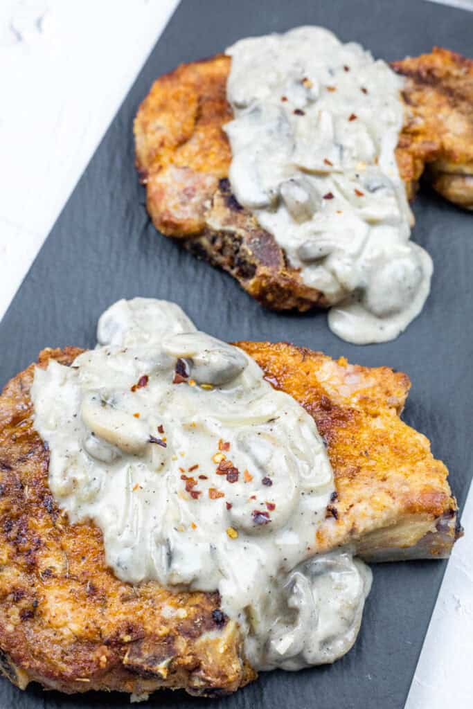 Serving of Cast Iron Smothered Pork Chops in a black rectangular plate.
