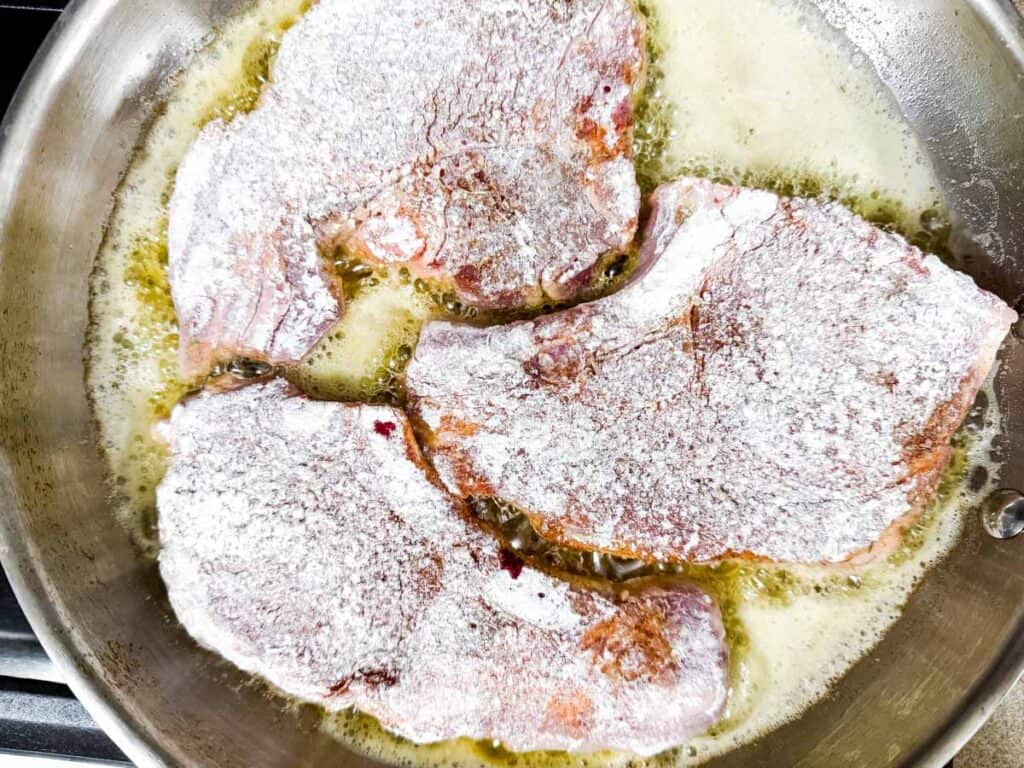 Coated pork chops cooking in a melted butter in a pan.