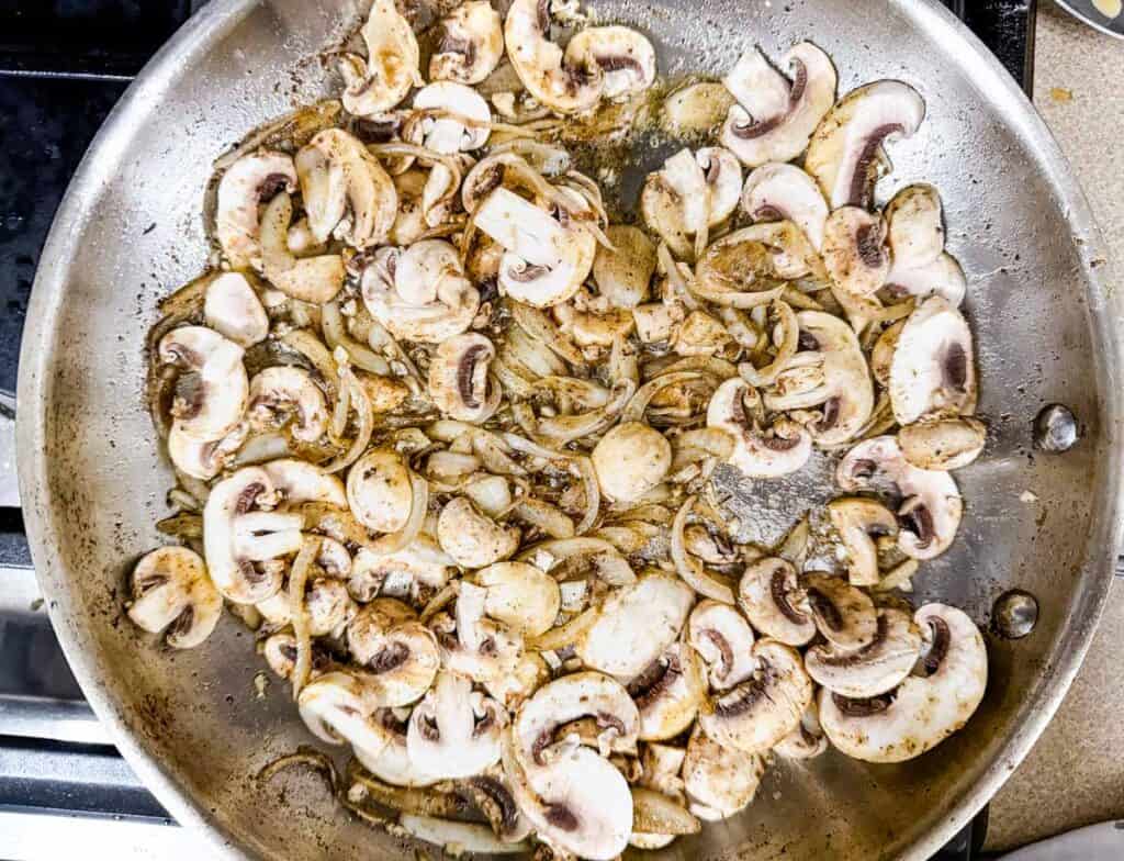 Cooking mushrooms, onions, and garlic in a pan on a stove.