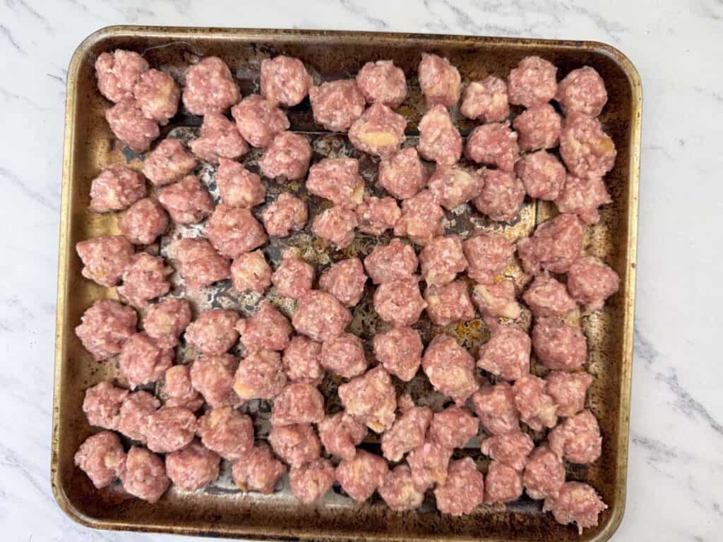 Raw mini meatballs arranged on a baking sheet, ready for cooking.