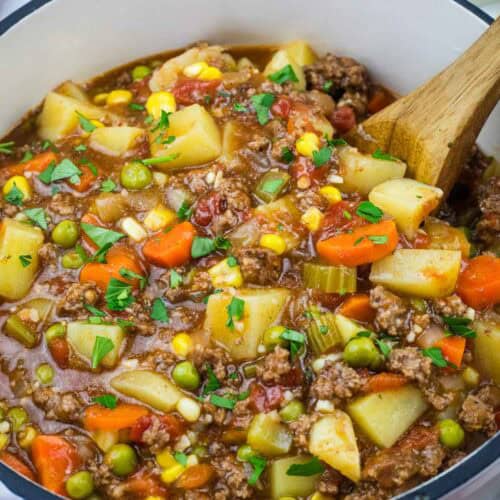 Mom&rsquo;s Hamburger Stew with potatoes, carrots, peas, corn, and tomatoes, garnished with herbs.