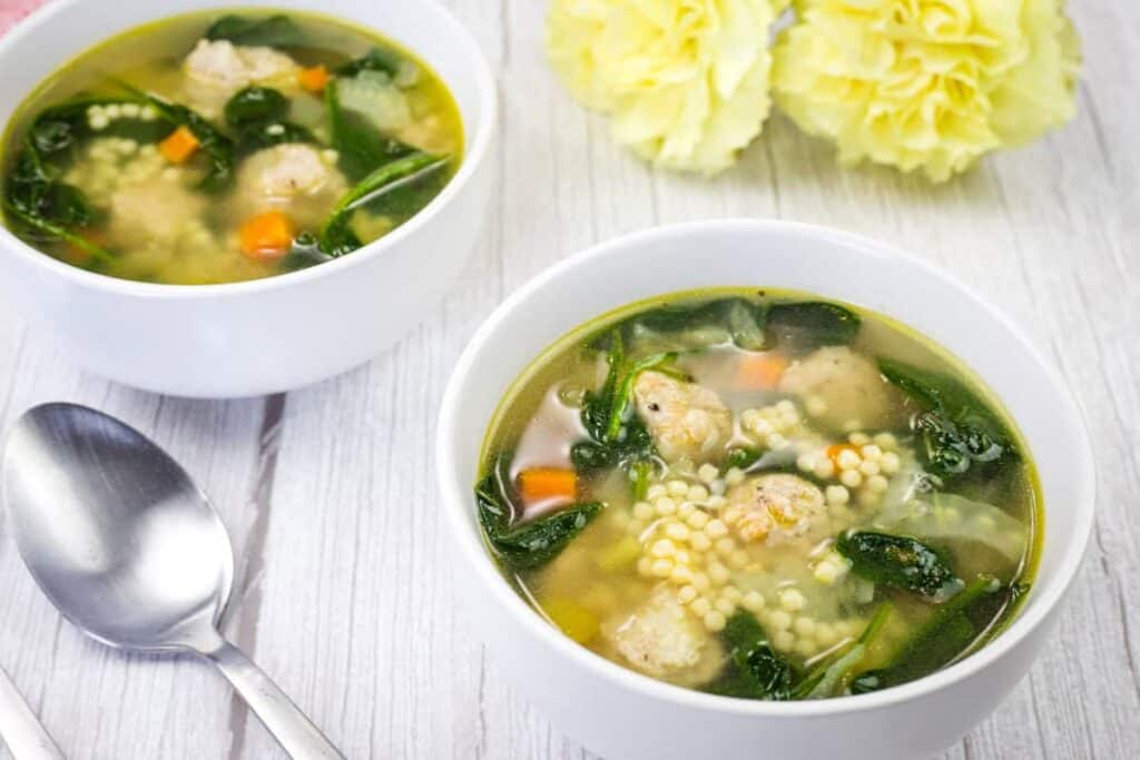 Two bowls of Italian soup accompanied by yellow flowers and a spoon.