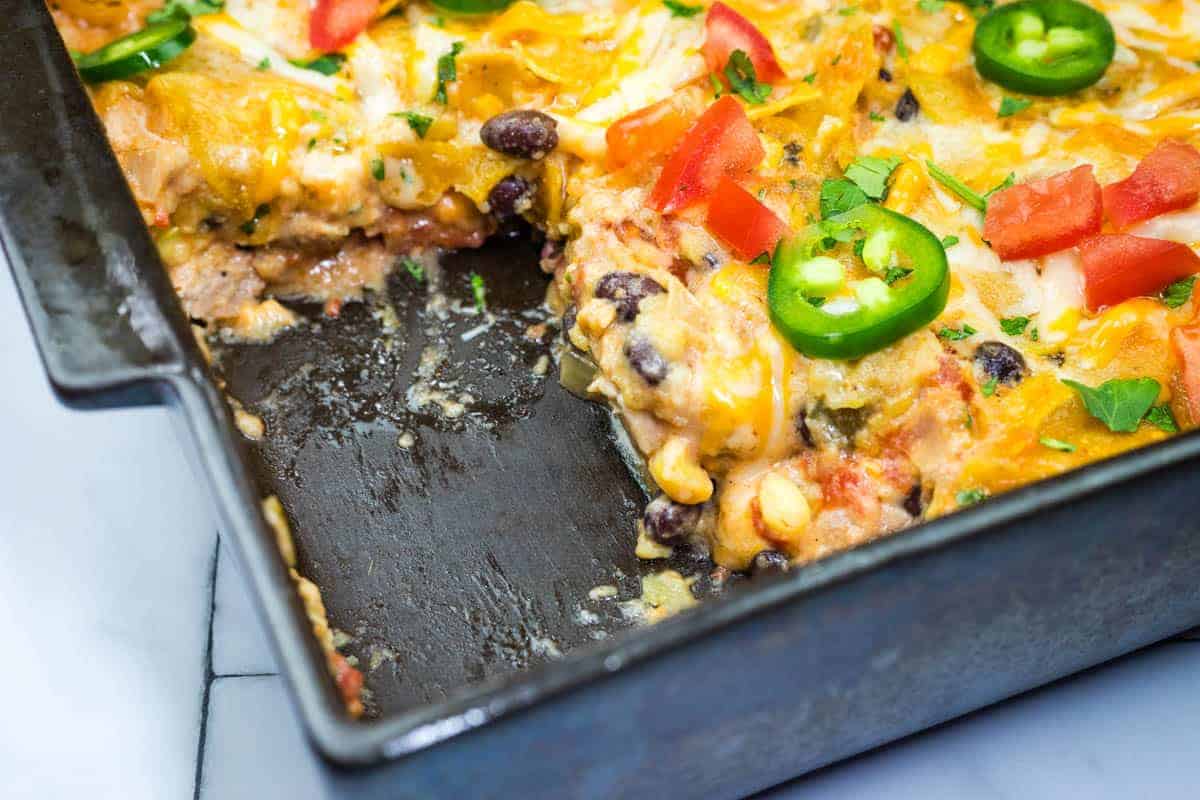 A close-up of a partially eaten cheesy Mexican chicken casserole in a baking dish.