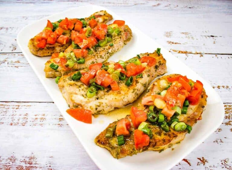 Three pork chops with tomato and green onion on a white plate.