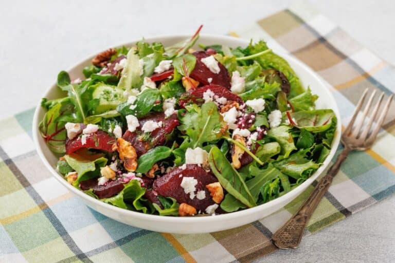 A bowl of salad with mixed greens, beet slices, walnuts, and crumbled goat cheese.