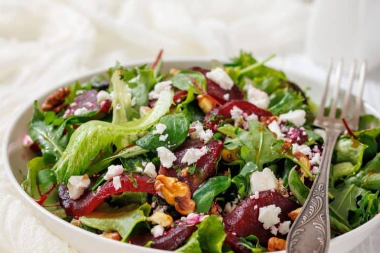 A bowl of mixed green salad with beet slices, crumbled feta cheese, and walnuts.