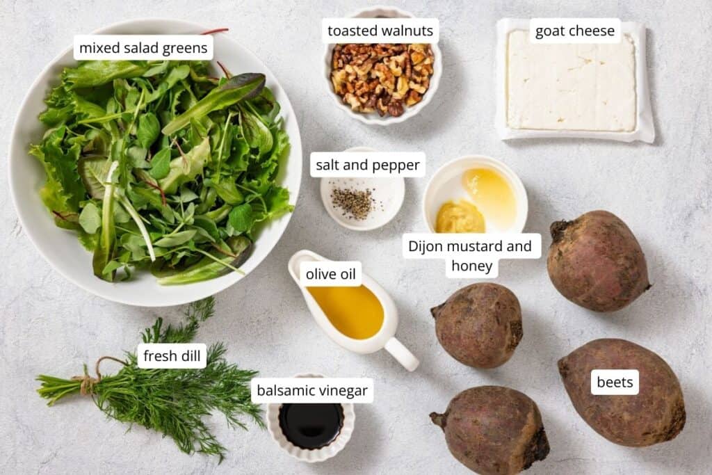 Ingredients for a salad: mixed greens, toasted walnuts, goat cheese, beets, fresh dill, olive oil, balsamic vinegar, Dijon mustard and honey, salt, and pepper on a light surface.