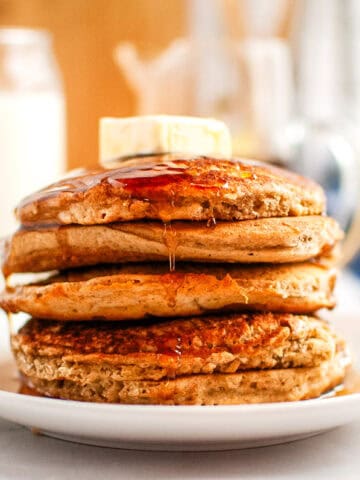 A stack of Buttermilk Oatmeal Pancakes with syrup and a pat of butter on top, served on a white plate.