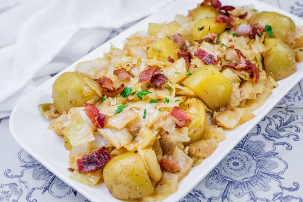 A dish of Cabbage & Potatoes with Bacon garnished with parsley on a white platter.