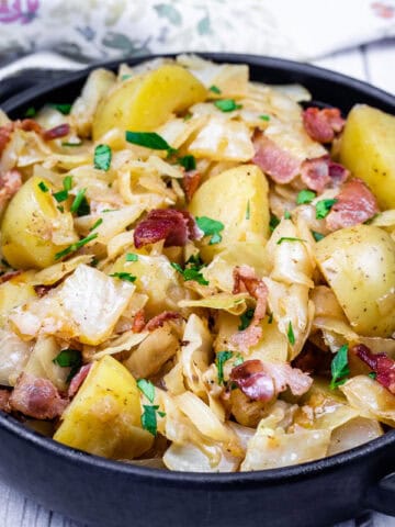 A black bowl filled with Cabbage and Potatoes with Bacon.