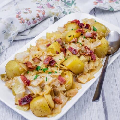 A dish of Cabbage & Potatoes with Bacon garnished with herbs on a rectangular white plate.