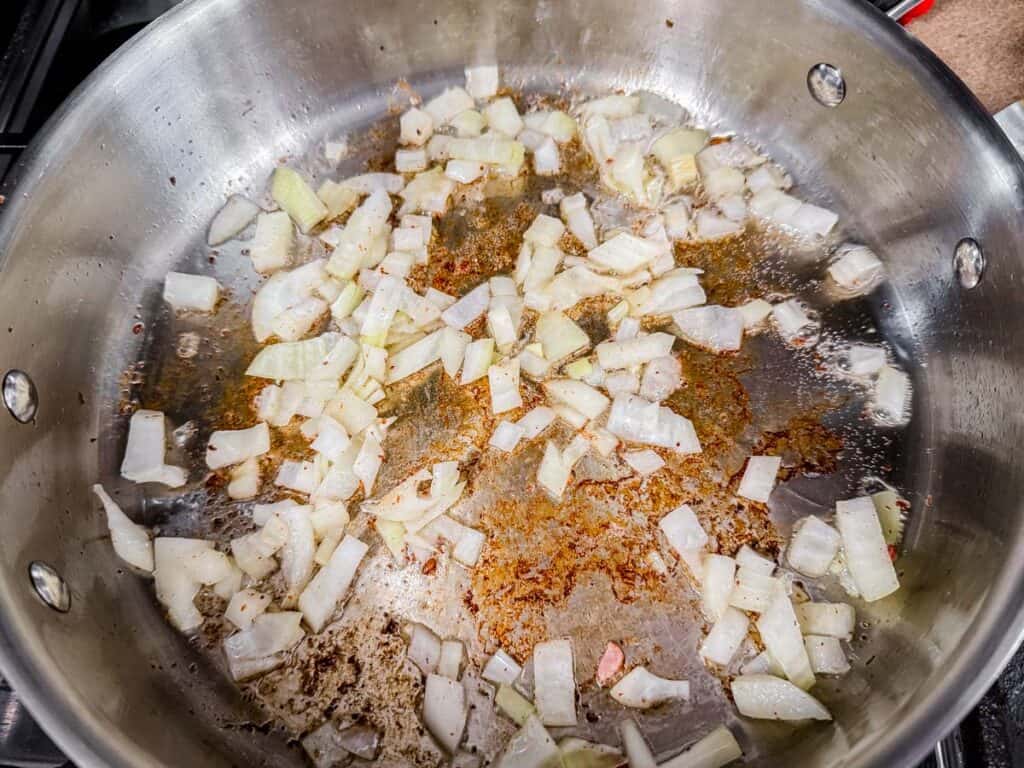 Chopped onions cooking in a stainless steel pan with browned bits on the surface.
