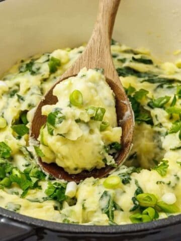 A pot of Colcannon with Kale, with a wooden spoon lifting a portion.