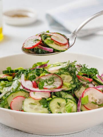 A white bowl filled with Radish Salad. A spoon is holding a portion above the bowl.