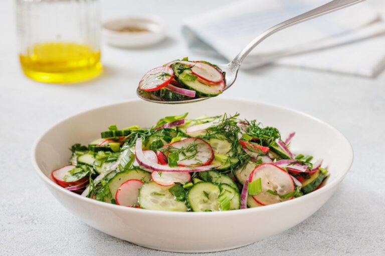 A white bowl filled with Radish Salad. A spoon is holding a portion above the bowl.